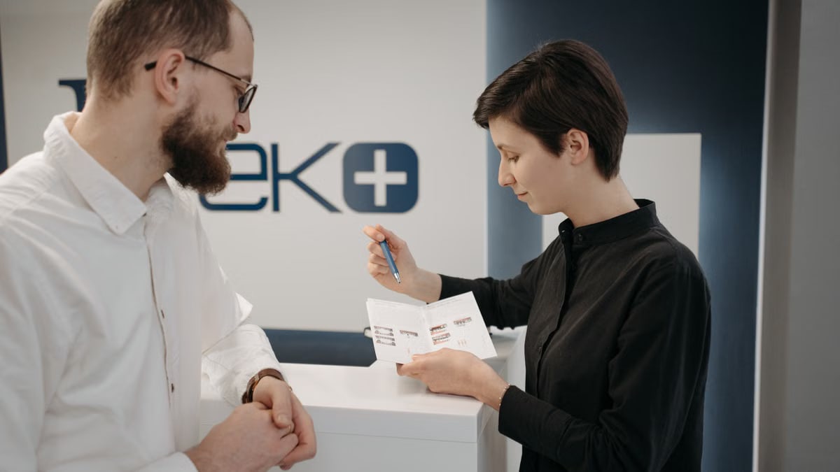 Customer discussing information sheet with receptionist in clinic.